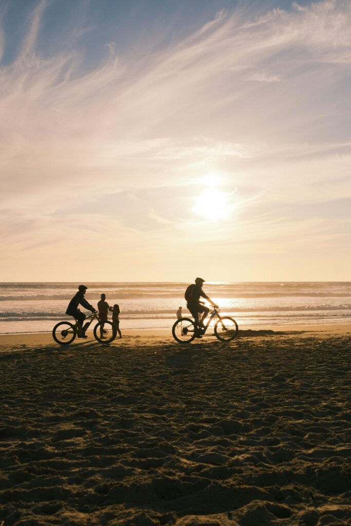 Cyclists ride along the sandy beach of Costa da Caparica, Portugal, silhouetted against a stunning sunset.